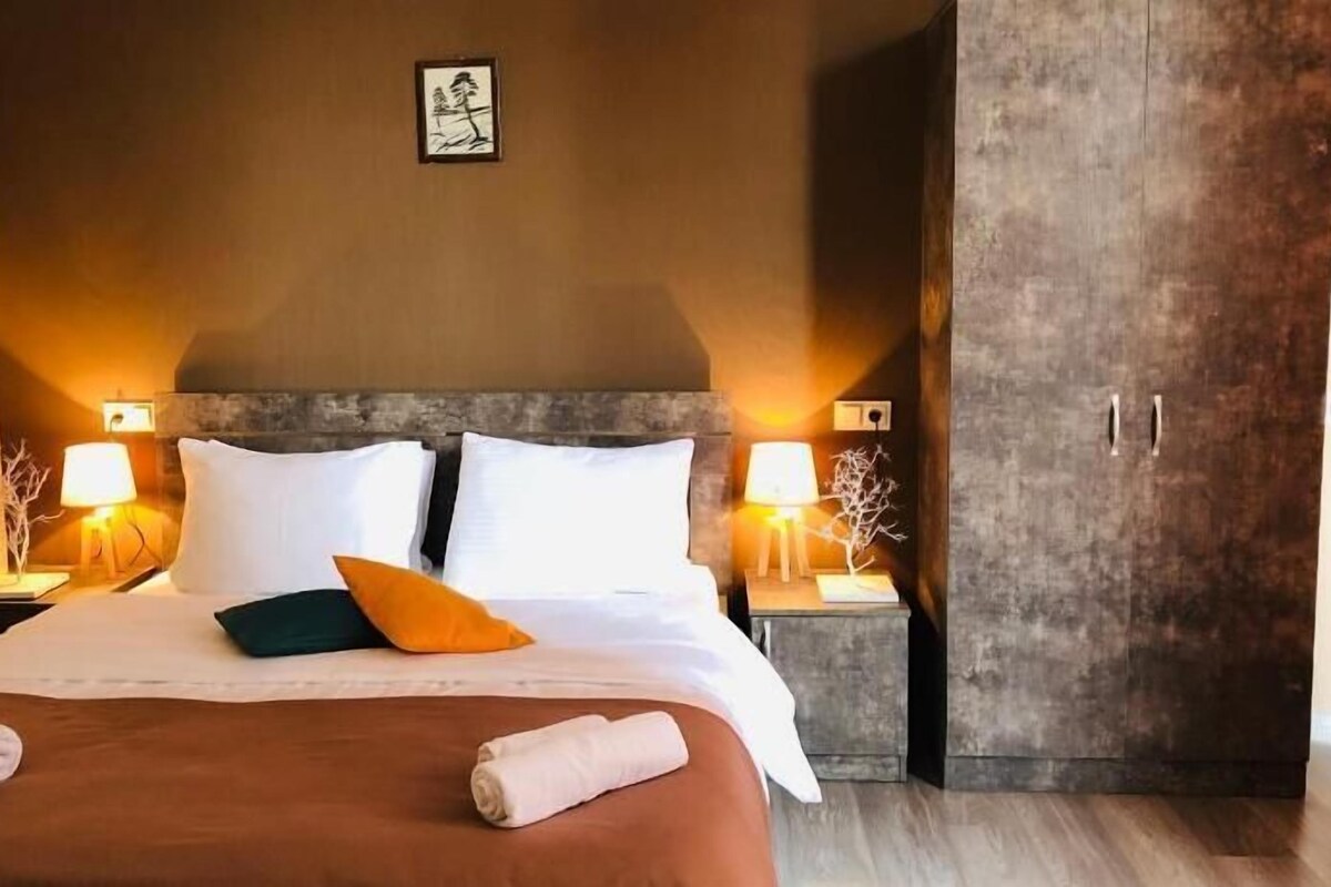 A hotel room with a large bed, two bedside tables with lamps, a wardrobe, and a small picture on the wall.