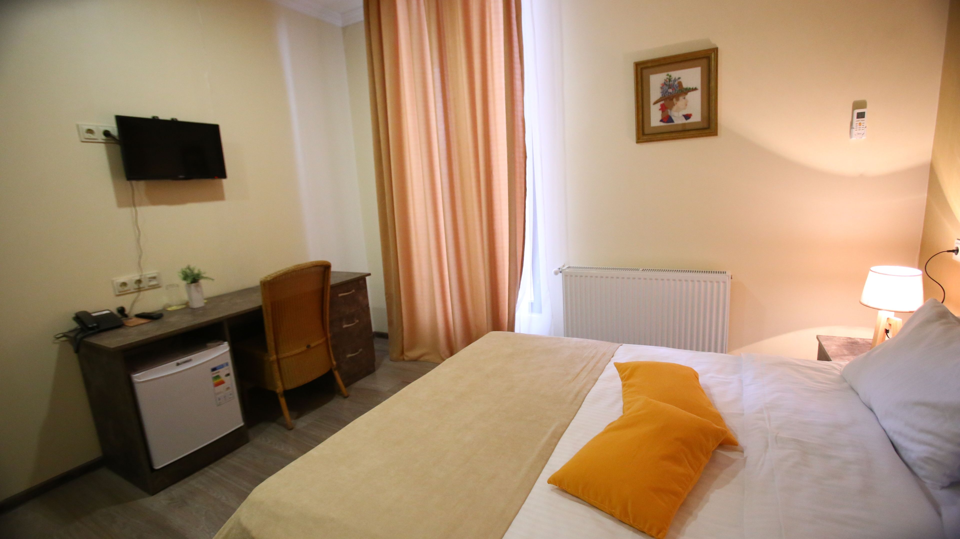 Quarto de hotel com cama, escrivaninha com computador, cadeira, televisão fixada na parede e janela com cortinas.