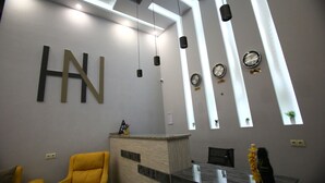 Et moderne receptionsområde med et stort 'HN'-skilt, en receptionsdisk, en gul lænestol og en plante på disken.
