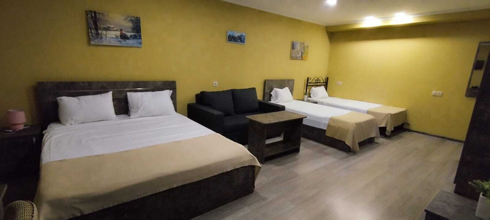 A hotel room with a large bed, a sofa, two smaller beds, and a small table.