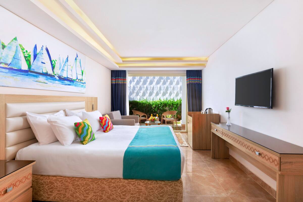 Een hotelkamer met een groot bed, een bureau, een televisie en een schilderij van zeilboten.