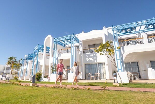 A hotel with white and blue architecture, featuring balconies and a well-maintained lawn.