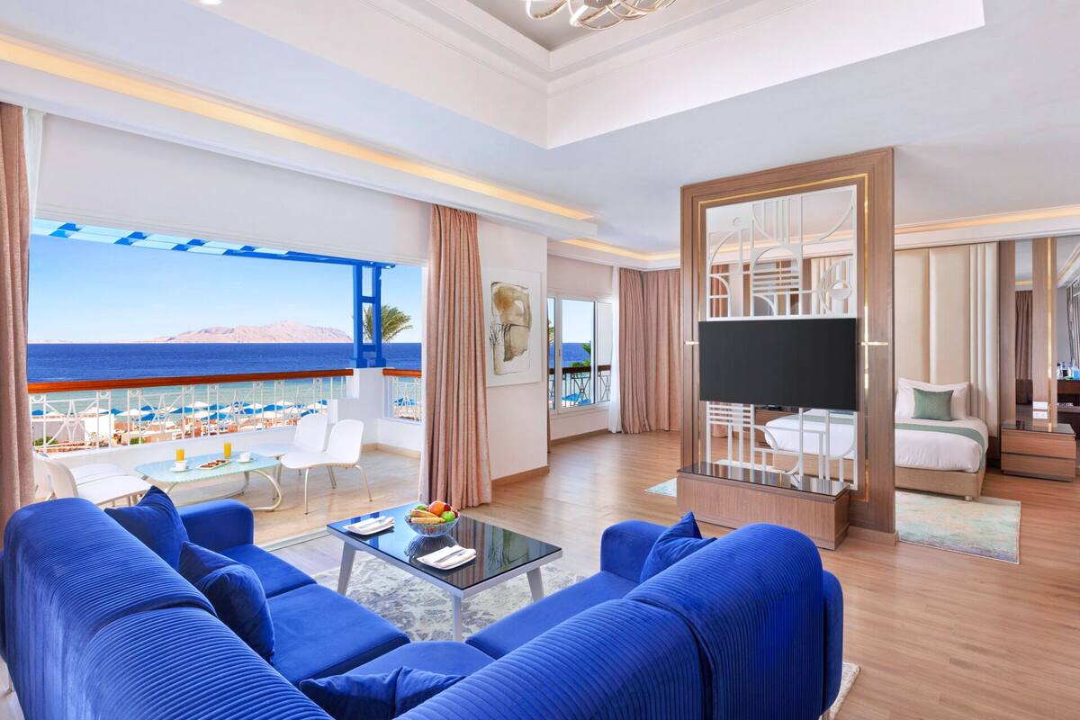 Een ruime woonkamer met een grote zithoek, een flatscreen-tv en een balkon met uitzicht op zee.