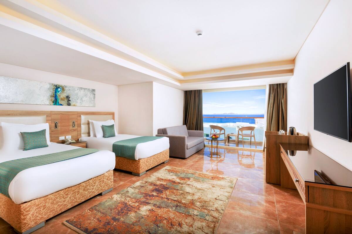 Een hotelkamer met twee bedden, een bureau, een televisie en uitzicht op zee.