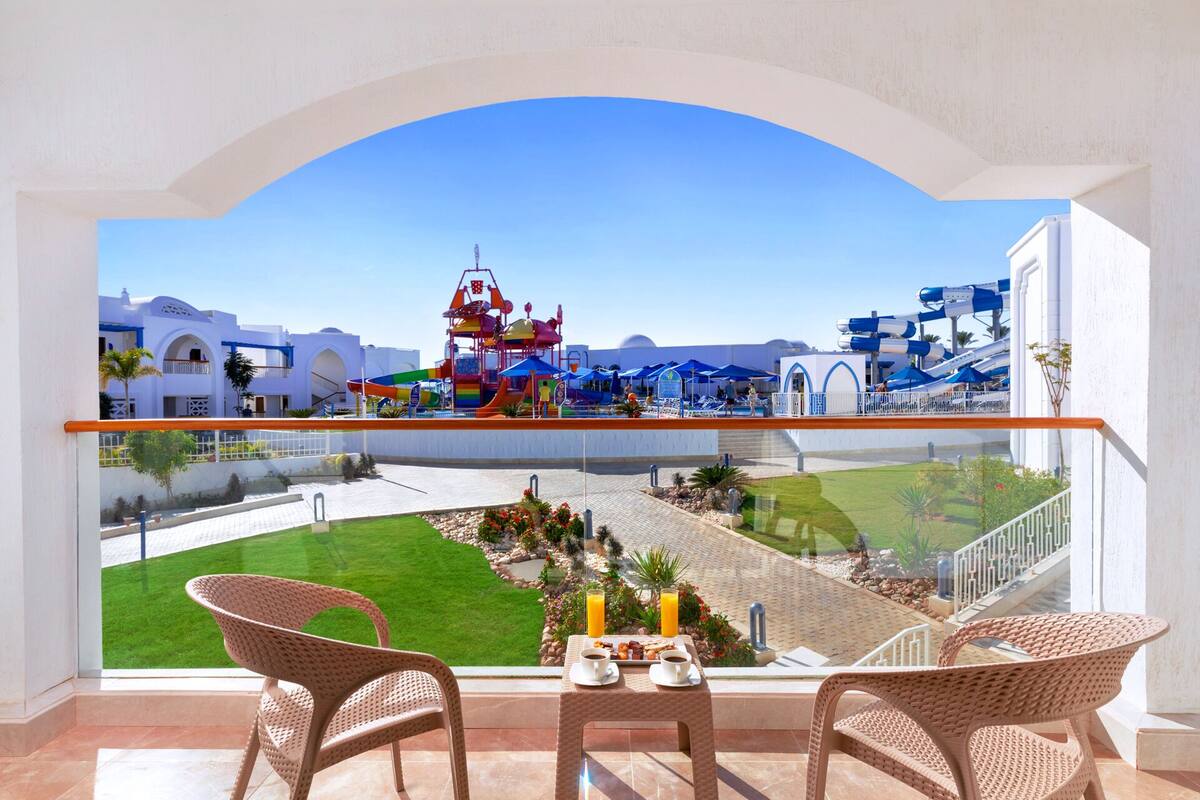 Een balkon met rieten stoelen, een tafel met ontbijt en uitzicht op een waterpark en zwembad.