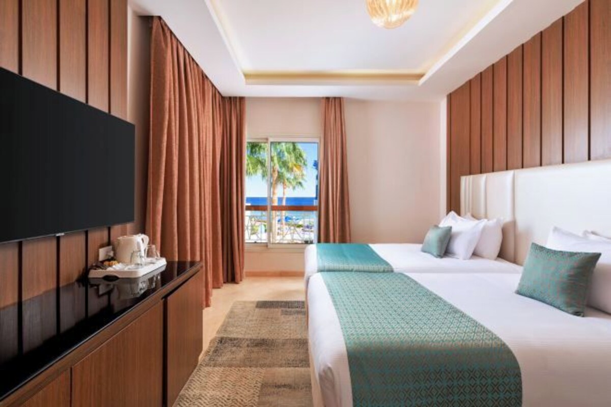 Een hotelkamer met een bed, een televisie, een bureau en uitzicht op het strand.