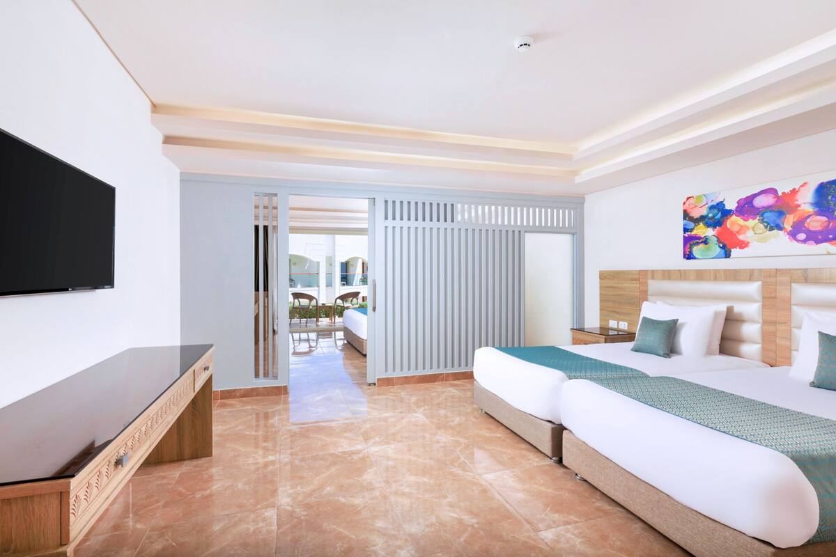 Hotelkamer met een groot bed, een flatscreen televisie, een houten nachtkastje en uitzicht op het buitengebied door een schuifdeur.