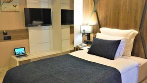 Ein Hotelzimmer mit Bett, Schreibtisch, Laptop, Fernseher und Nachttisch mit Lampe.