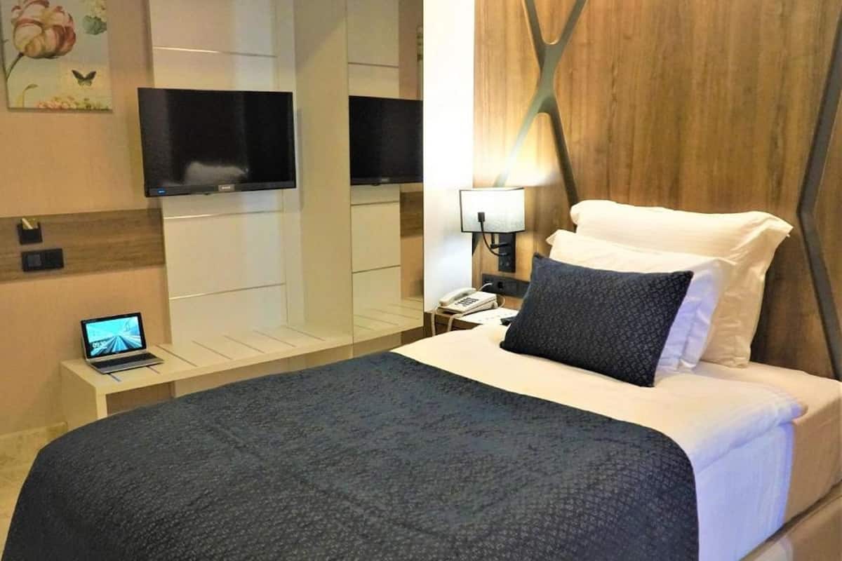 A hotel room with a bed, a desk with a laptop, a TV, and a nightstand with a lamp.