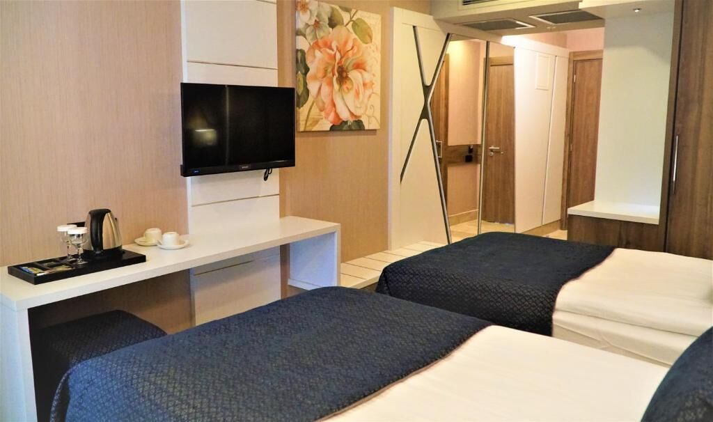 Una habitación de hotel con cama, mesita de noche, televisor y un cuadro.