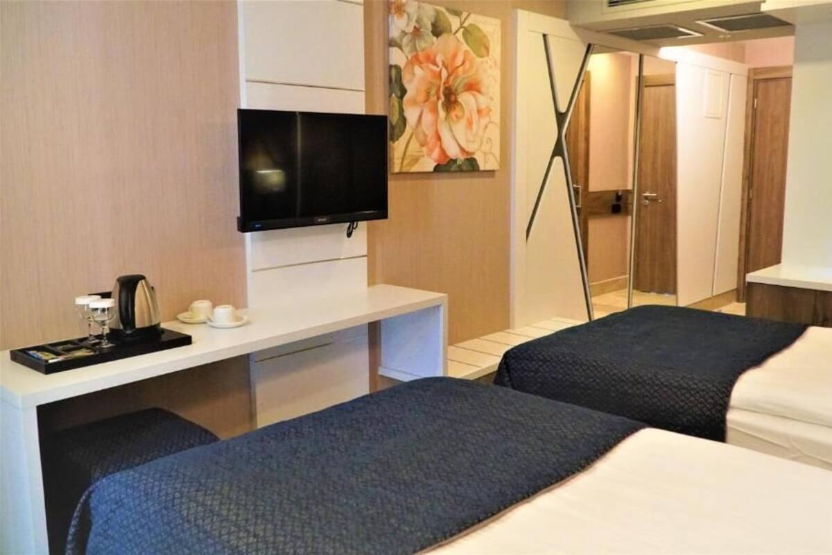A hotel room with a bed, bedside table, TV, and a painting.