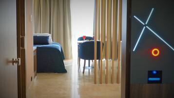 A hotel room with a bed, a chair, and a table with a glass of red drink.
