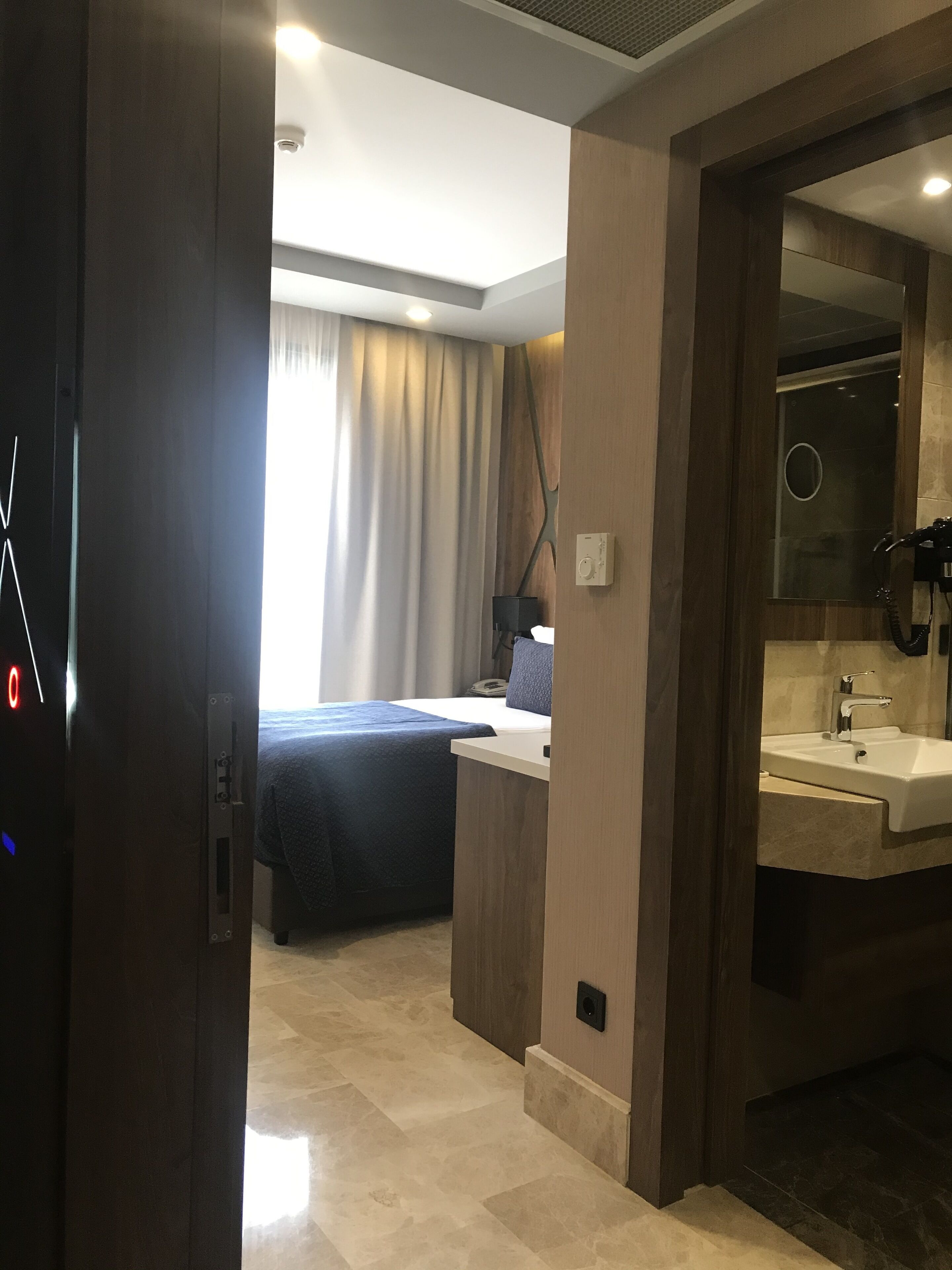 A hotel room with a bed, a desk, a bathroom with a sink, and a mirror.