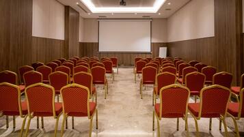 Un salón de conferencias con hileras de sillas rojas y una pantalla grande al frente.