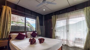 A bedroom with a large bed, wooden headboard, and a view of a rocky landscape through a window. - Kanya Cozy Bungalows Kata Beach (Karon)