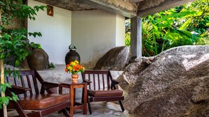 A wooden bench and table set against a wall with a large rock. - Kanya Cozy Bungalows Kata Beach (Karon)