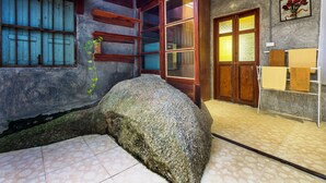 A traditional room with a large rock, a wooden door, and a window with blue shutters. - Kanya Cozy Bungalows Kata Beach (Karon)
