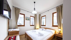 Una habitación de hotel con cama, mesitas de noche, televisor y ventanas con cortinas.