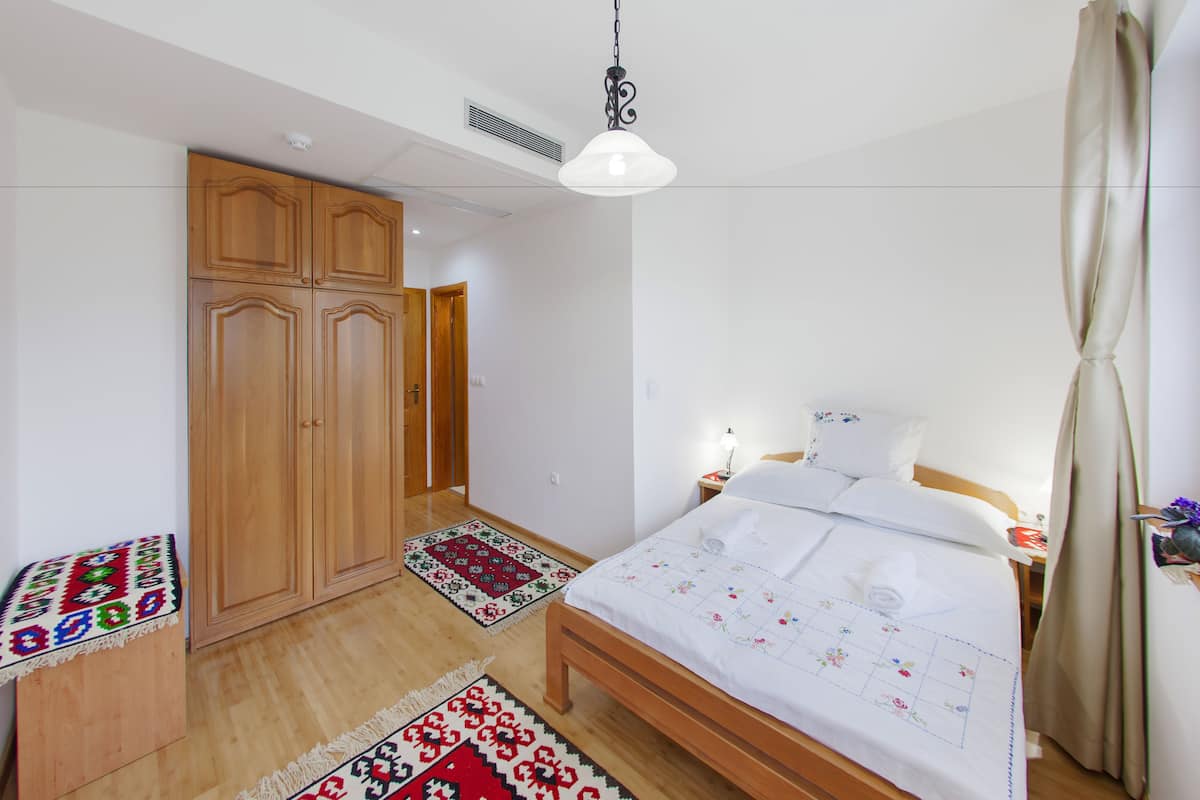 A bedroom with a bed, wooden wardrobe, and a nightstand with a lamp.