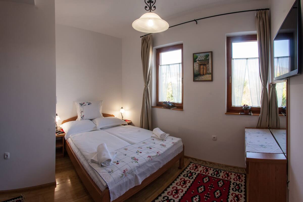 A bedroom with a bed, nightstands, a desk, and a window with curtains.