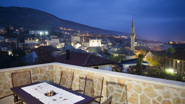 Un balcón de piedra con una mesa preparada para comer, con vistas a un pueblo con edificios históricos y una torre destacada.