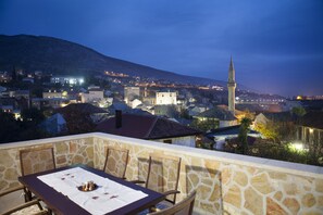 Un balcón de piedra con una mesa preparada para comer, con vistas a un pueblo con edificios históricos y una torre destacada.