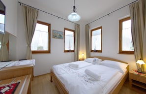 Une chambre d’hôtel avec un lit double, un bureau et une chaise. Il y a deux fenêtres avec des rideaux, un tableau au mur et une lampe sur la table de chevet.