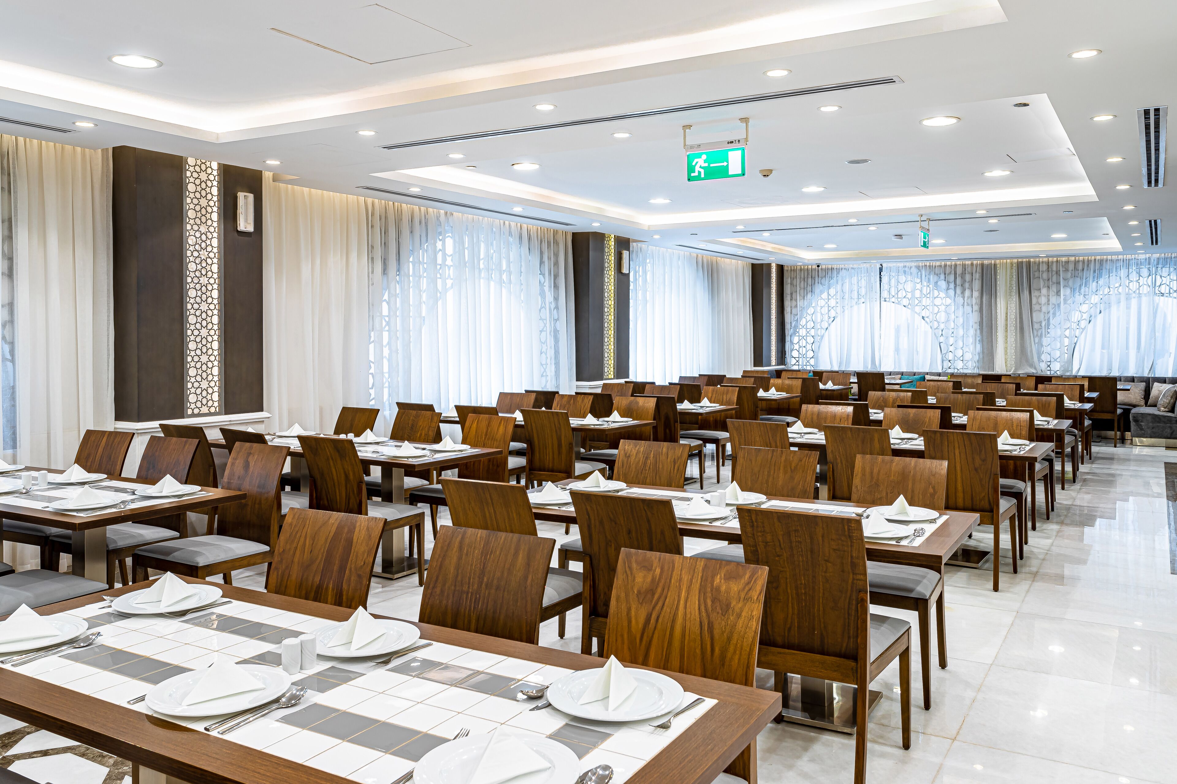 A spacious conference room with rows of wooden tables and chairs, equipped with nameplates and place settings.