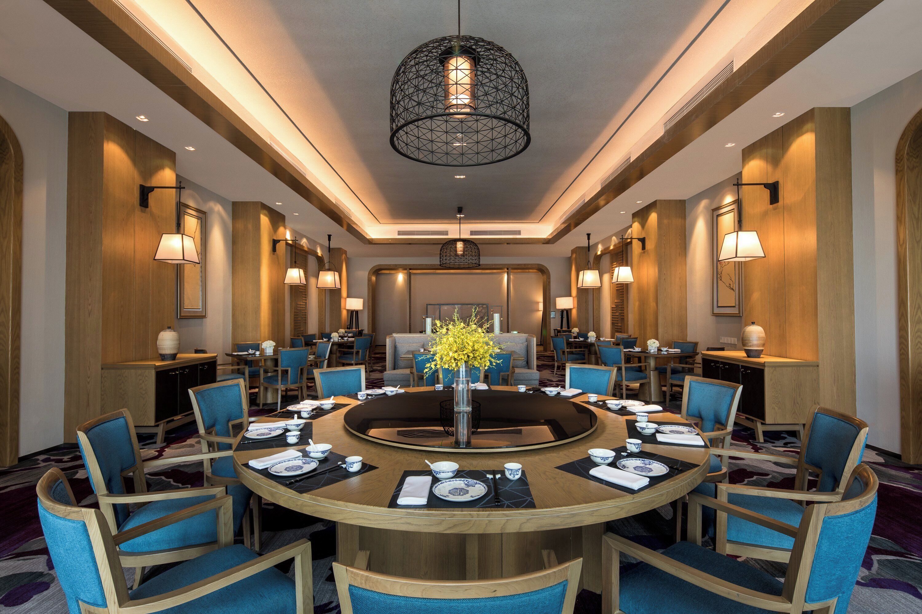 A hotel dining area with a round table set for a meal, surrounded by chairs, and a central decorative plant.