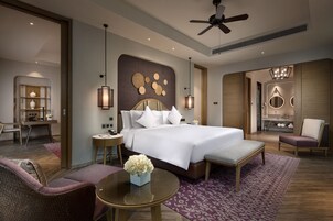 A modern hotel room with a large bed, a desk, a chair, a round table, and a ceiling fan.
