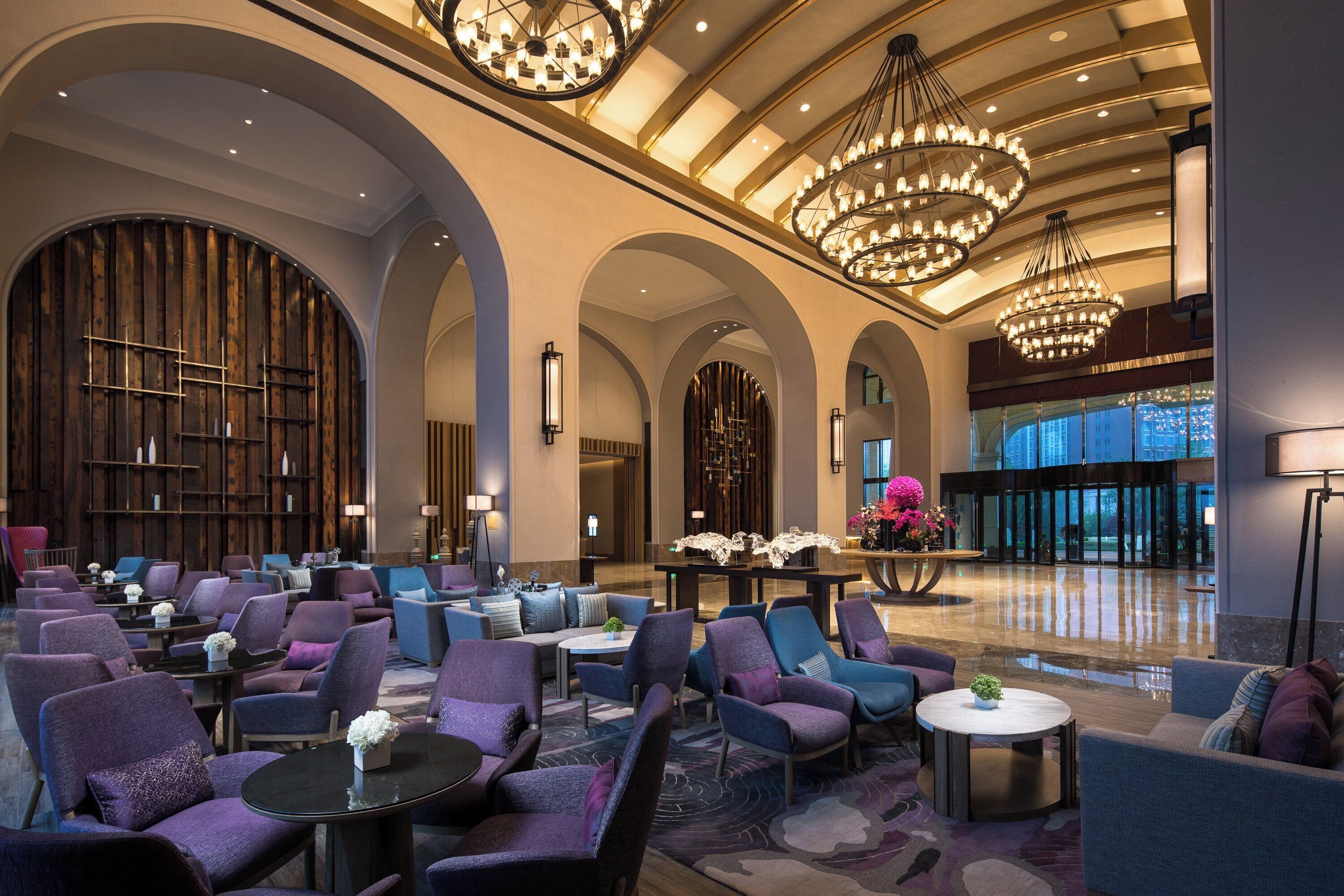A spacious lobby with multiple seating areas, large chandeliers, and a modern interior design.