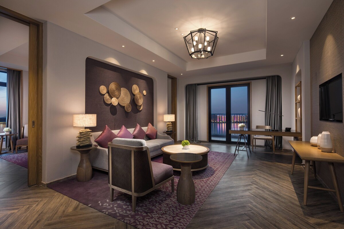 Une chambre d’hôtel moderne, dotée d’un canapé, d’un fauteuil, d’une table basse ronde et d’un coin repas avec une table et des chaises.