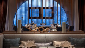A modern interior with a seating area, a large window with a geometric design, and a decorative wooden piece. - Crowne Plaza Qingdao Oriental Movie Metropolis by IHG (Qingdao)