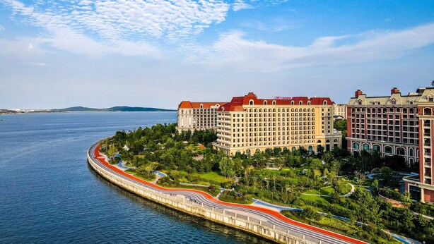 A coastal hotel with a red-roofed building, a marina, and a curved road leading to the hotel. - Crowne Plaza Qingdao Oriental Movie Metropolis by IHG (Qingdao)