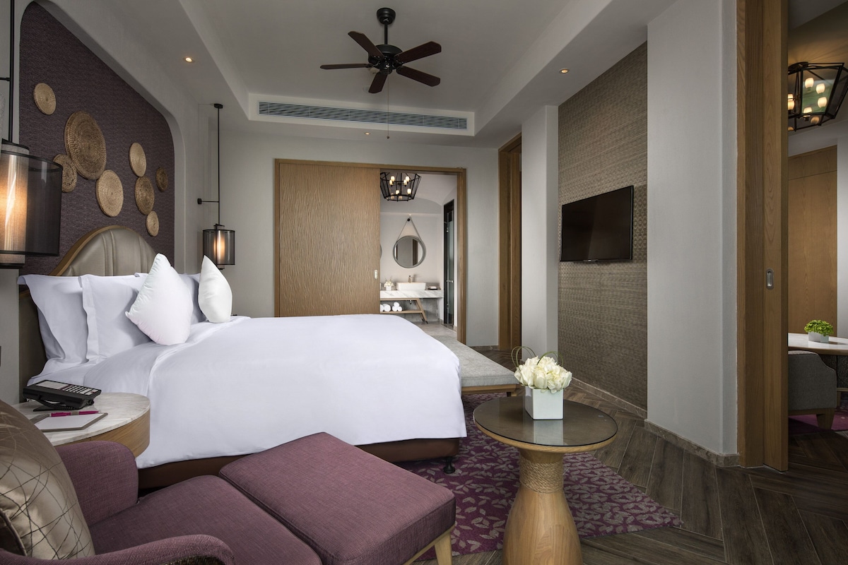 Une chambre d’hôtel avec un grand lit, un ventilateur de plafond, une télévision, un bureau et un coin salon.