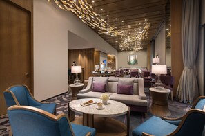 Un hall d’hôtel au design moderne, avec un espace de détente central comprenant des canapés et des fauteuils, une table basse ronde en marbre et un éclairage d’ambiance.
