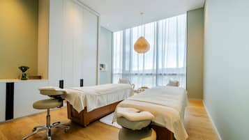 Two single beds with white linens, a wooden floor, and a large window.