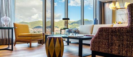 A spacious living room with a large window offering a city view, a modern chandelier, and a comfortable seating area.