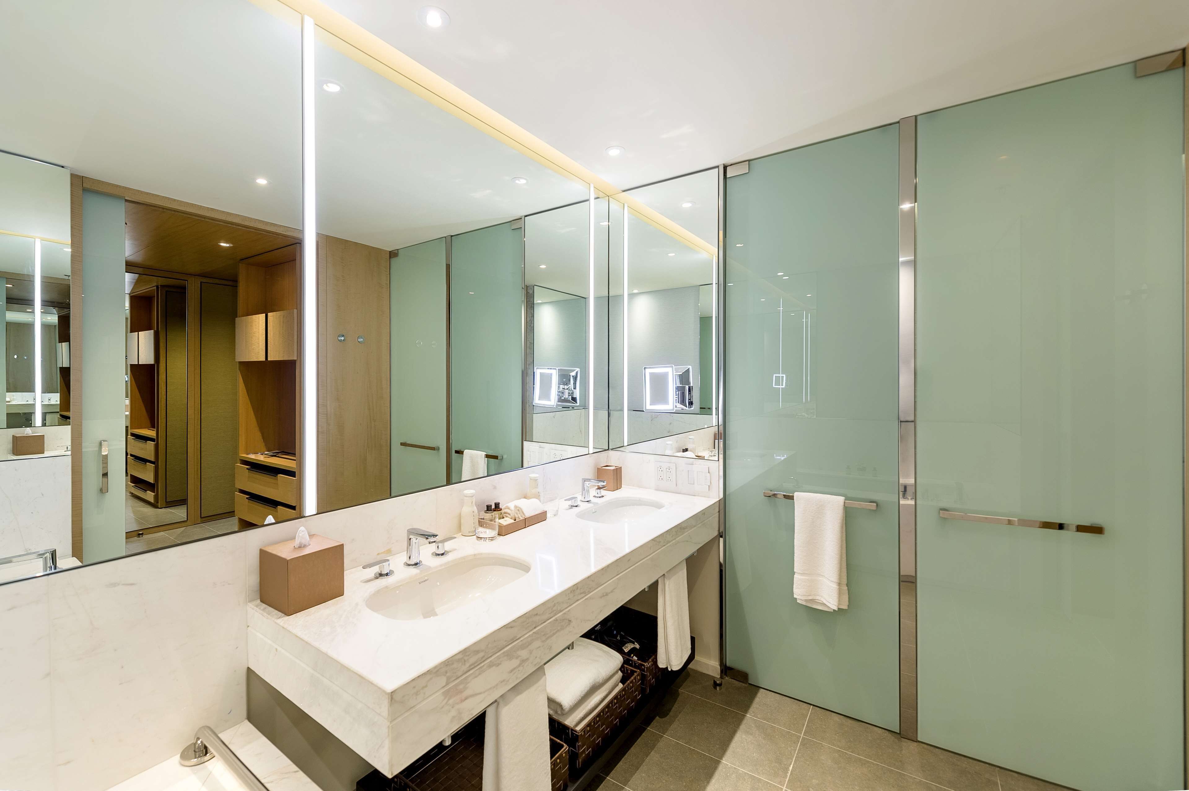 A modern bathroom with a long vanity, two sinks, a large mirror, and a glass shower enclosure.