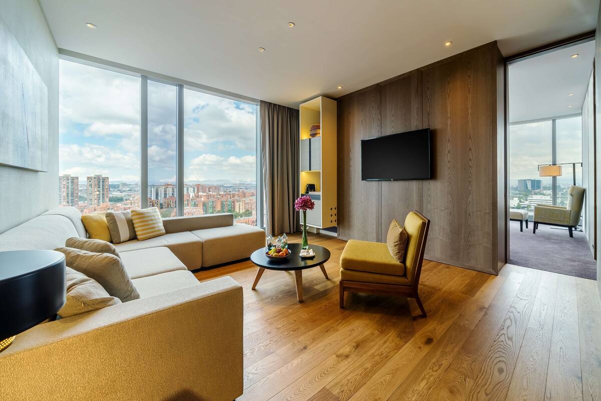 Ein modernes Wohnzimmer mit großem Fenster, einer Couch, einem Sessel, einem Couchtisch und einem an der Wand befestigten Flachbildfernseher.