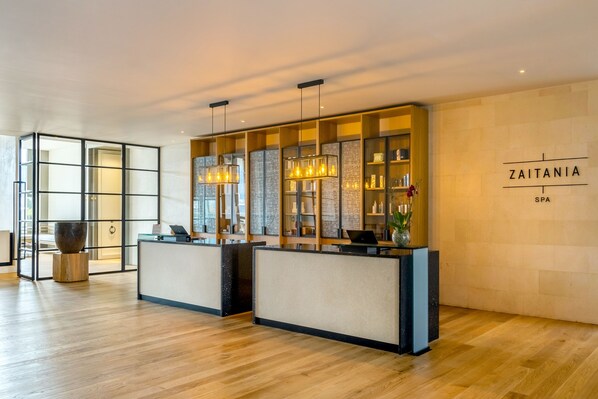 A reception area with wooden flooring, two reception desks, pendant lighting, and a wall with the name 'Zaitania SPA'.
