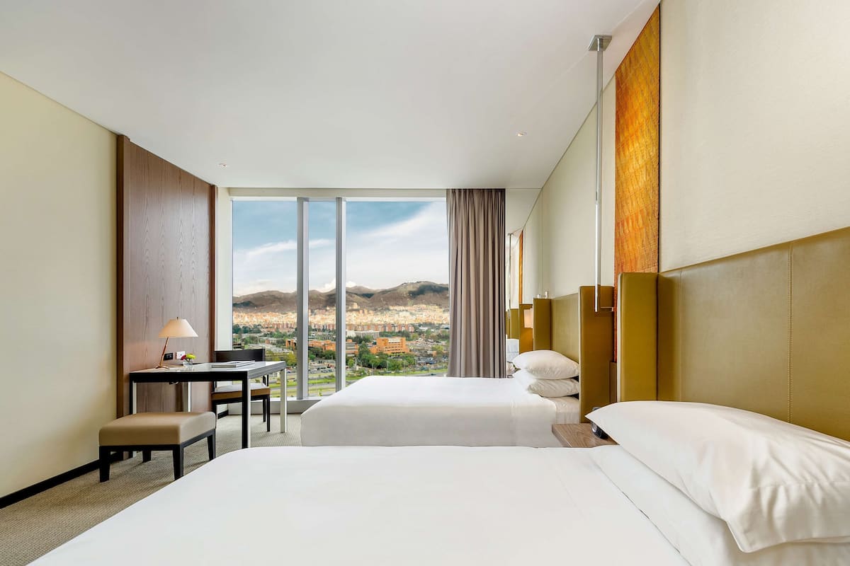 Ein Hotelzimmer mit zwei Betten, einem Schreibtisch und Blick auf eine Stadtlandschaft.