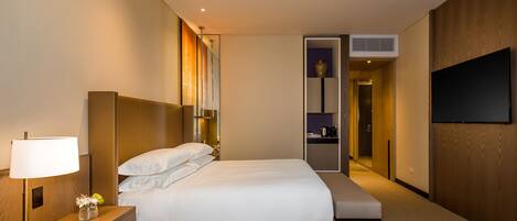 Habitación de hotel con una cama grande, mesita de noche, lámpara y televisor de pantalla plana montado en la pared.