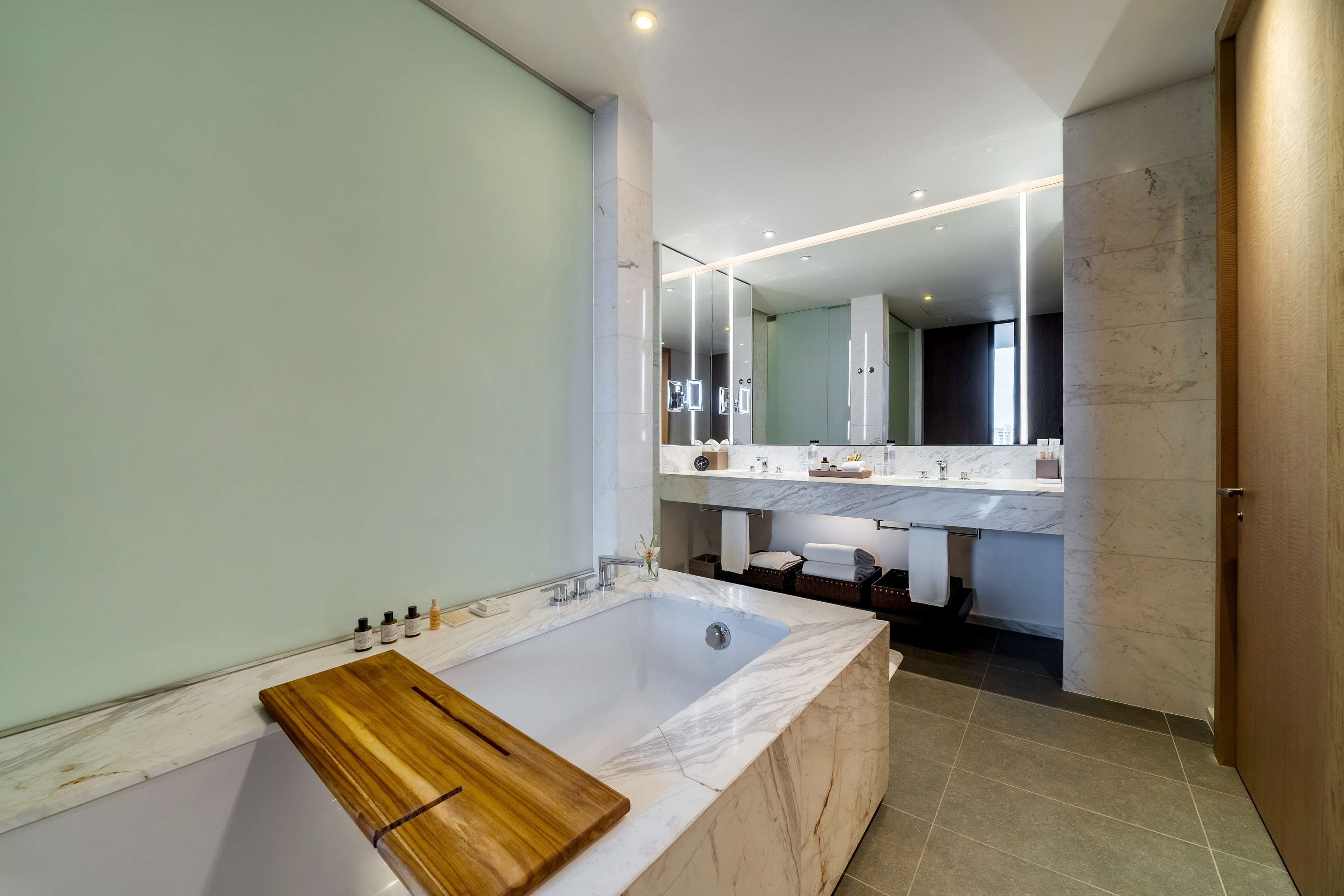 Une salle de bain moderne avec une grande baignoire, un plateau en bois, un meuble-lavabo en marbre et un miroir.