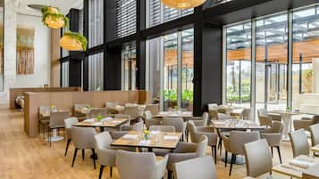 A modern restaurant with a high ceiling, large windows, and a mix of natural and artificial lighting.