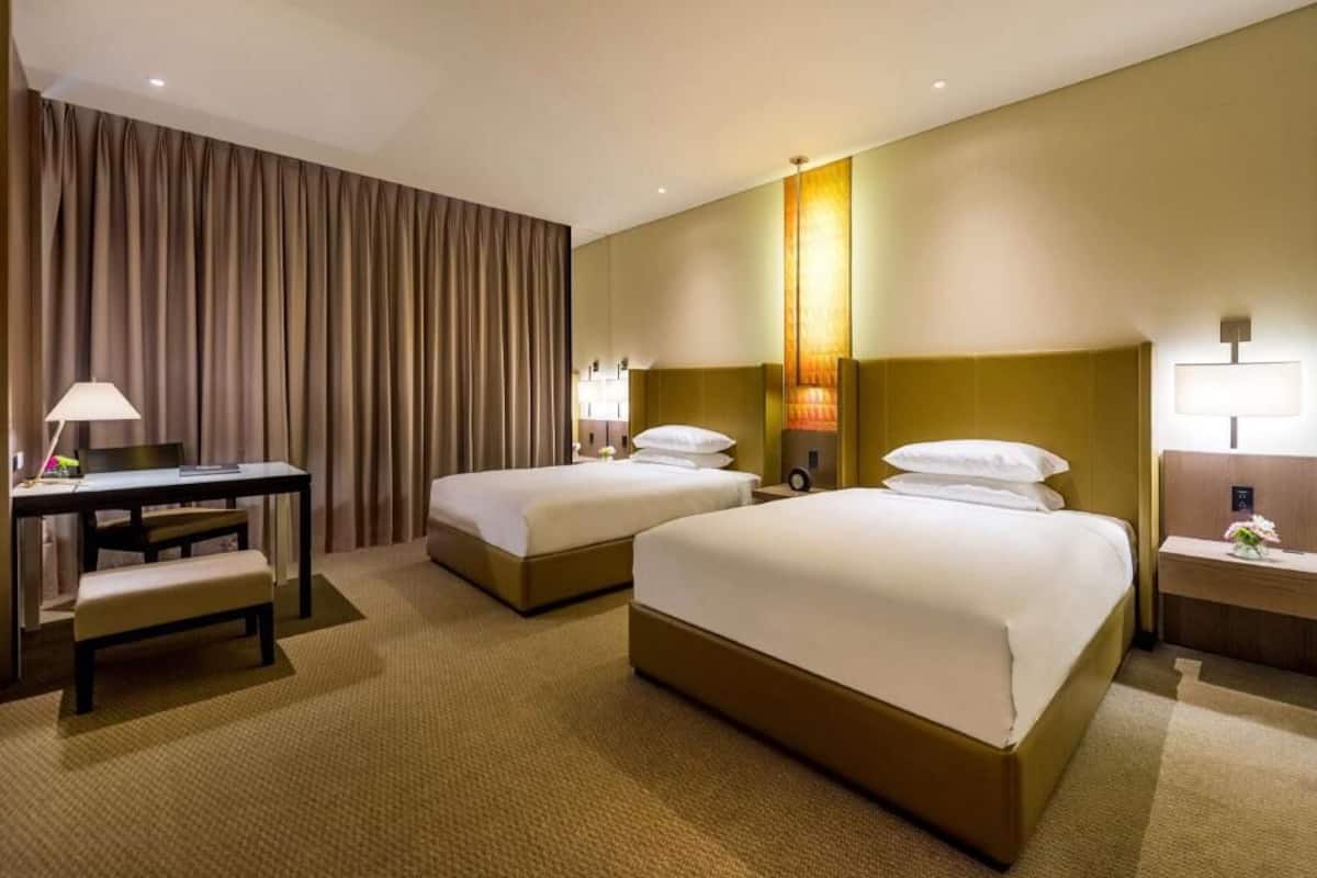 Une chambre d’hôtel avec deux lits, un bureau, une chaise et une table de chevet avec une lampe.