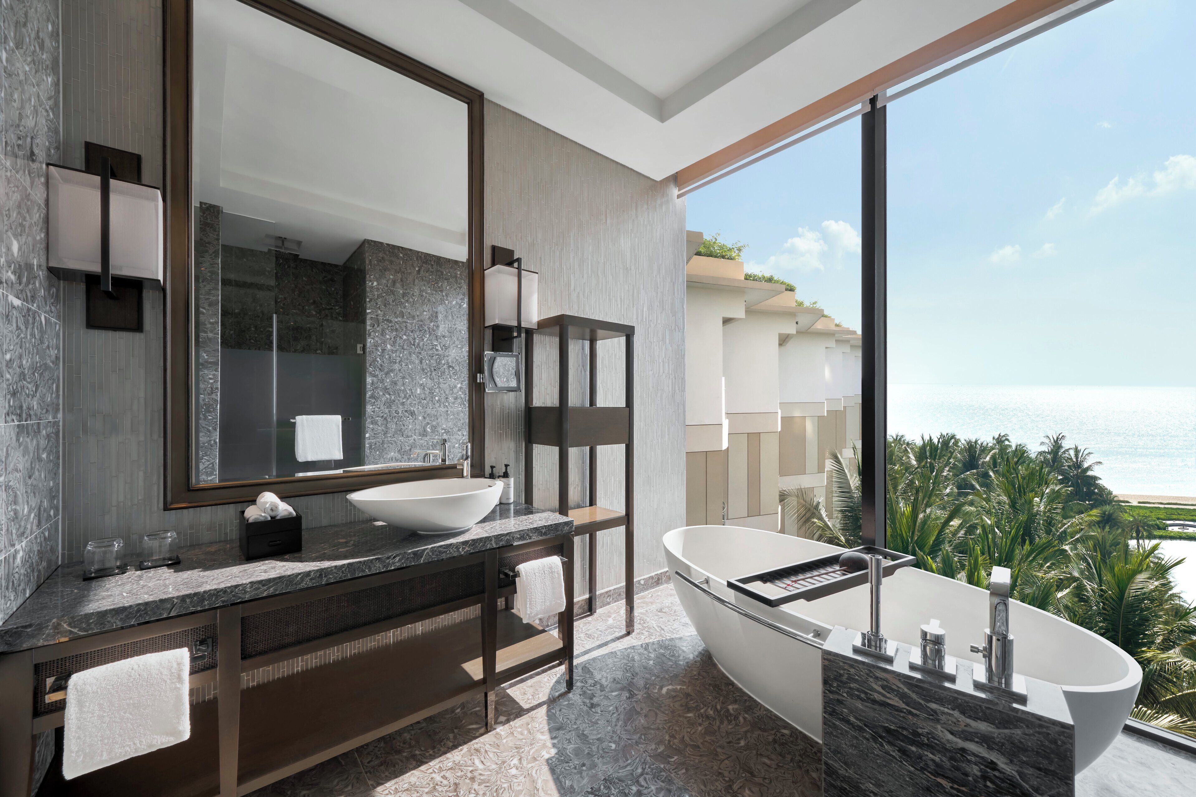 Un baño moderno con una bañera grande, un lavabo y un espejo. Cuenta con un ventanal con vistas al océano.