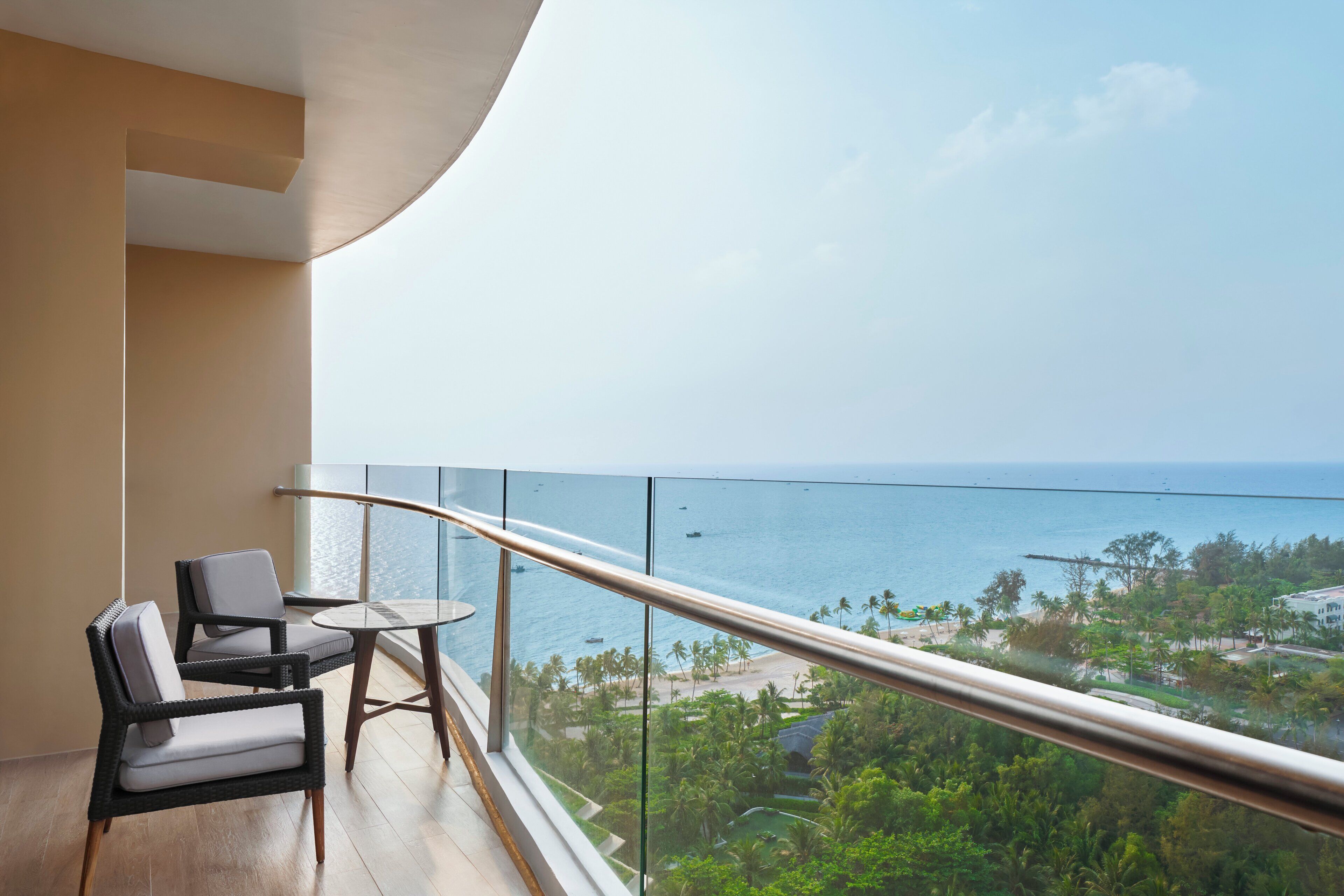 Ein Balkon mit Korbstühlen und einem kleinen Tisch, mit Blick auf einen Strand und den Ozean.