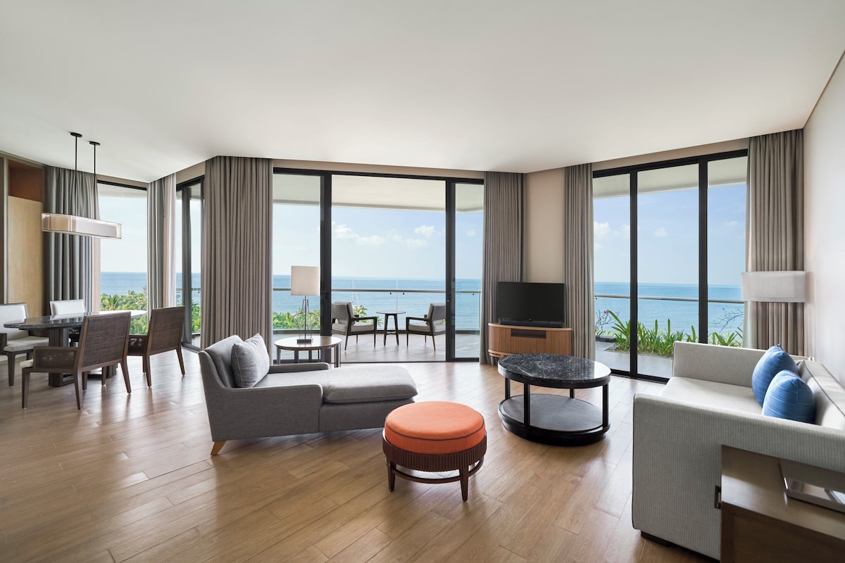 Una habitación de hotel moderna con balcón, sofá, zona de comedor y televisor.