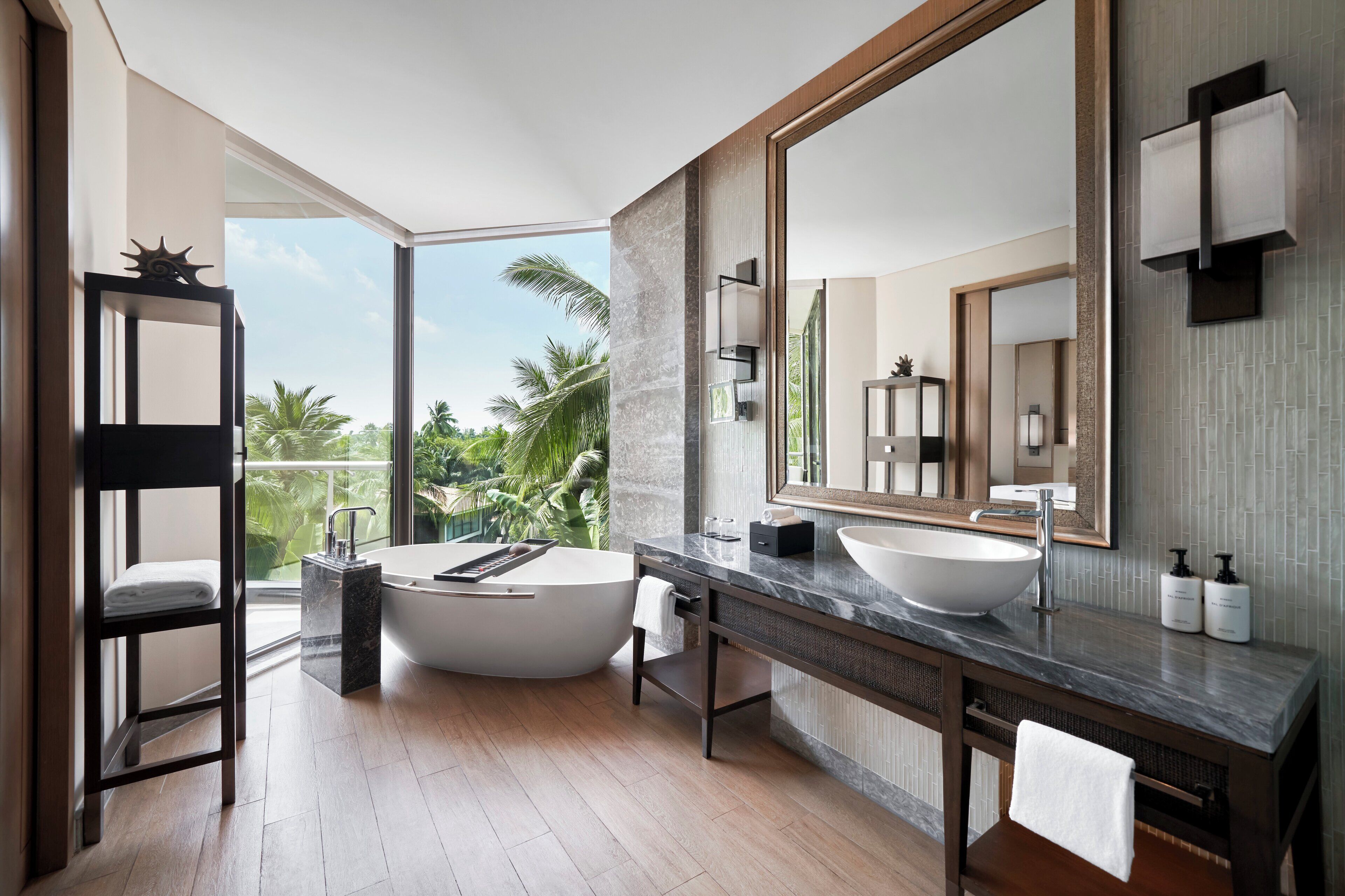 Une salle de bain moderne avec une baignoire sur pieds, un grand miroir et une vue sur des palmiers.